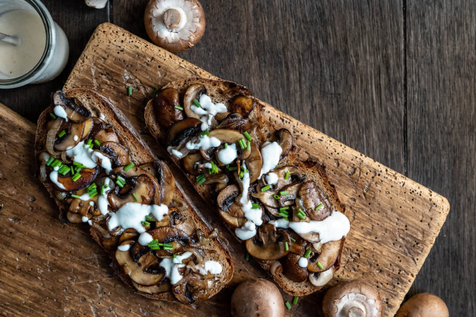 Schwarzwaldkruste Brot mit karamellisierten Zwiebeln und Pilzen angerichtet auf einem Holzbrett.