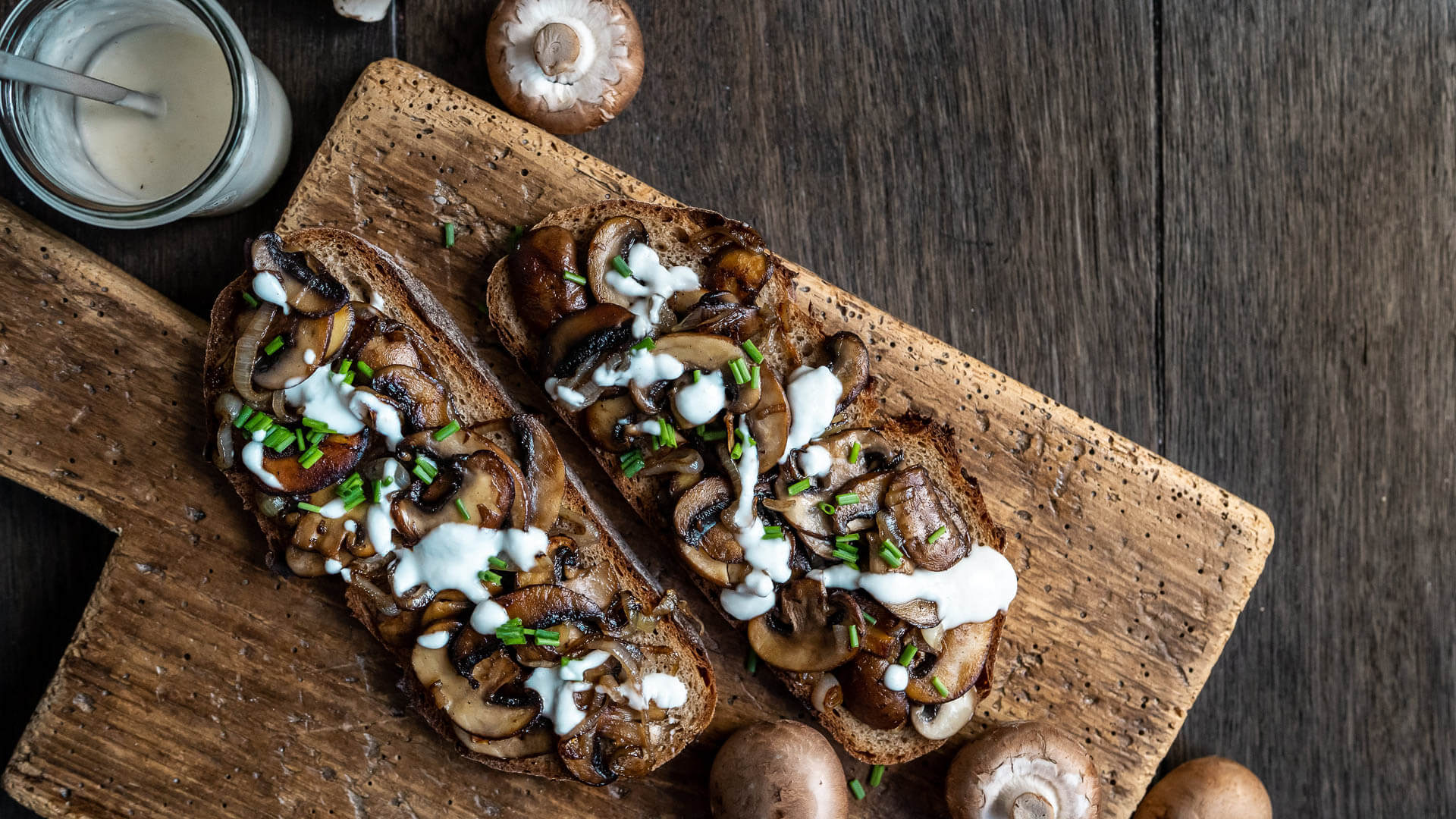 Schwarzwaldkruste Brot mit karamellisierten Zwiebeln und Pilzen angerichtet auf einem Holzbrett.